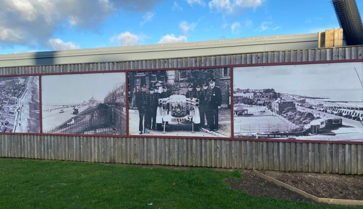 Four large prints of historic photographs, presented on hoardings on the Withernsea seafront. The prints depict an aerial view of Withernsea, the promenade with an early car, a group of uniformed men standing either side of a vintage car, and a scene of the seafront and sports courts.