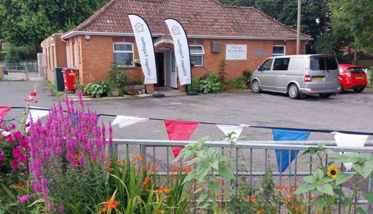 A single-storey red-brick building in a car park with bunting in the foreground.