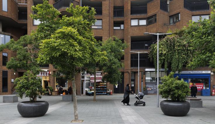 Gray stone planters planted with trees in a stone-paved area in between housing blocks.