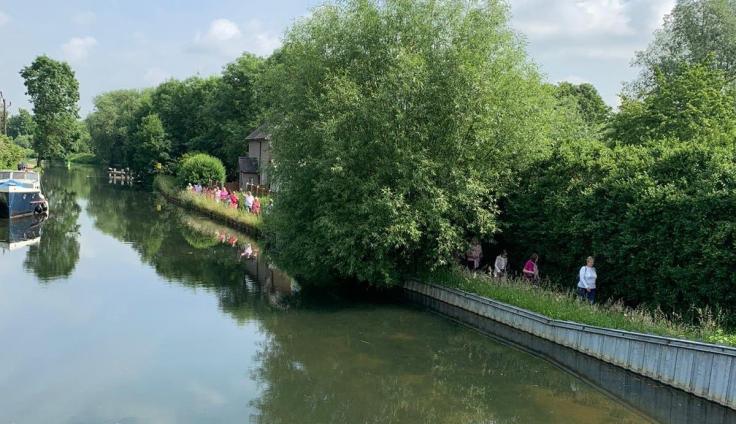 A group of more than ten people walking along a tree-lined path running alongside a canal.