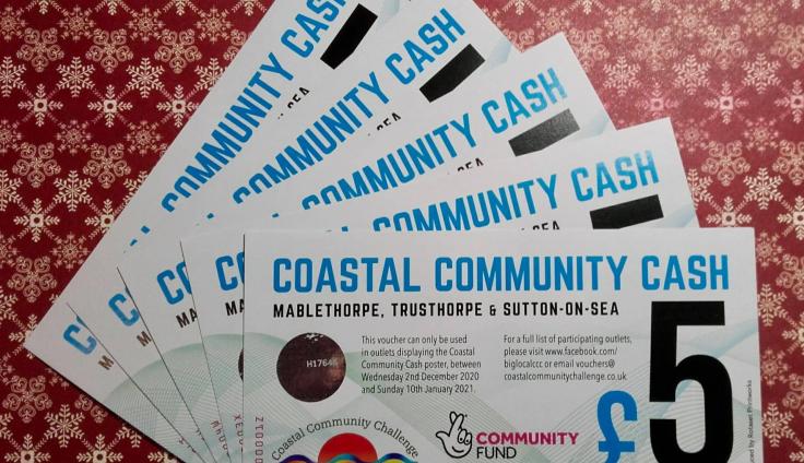 Five vouchers fanned out on a table each bearing the words "Coastal Community Cash £5."