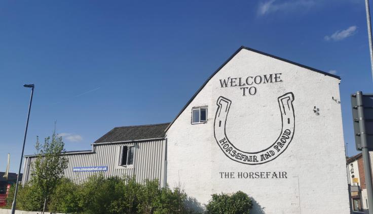 A white brick building with a large painted horseshoe and writing reading 'Welcome to The Horsefair'