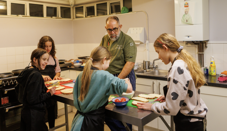Four young people and an adult making food on a table in a kitchen