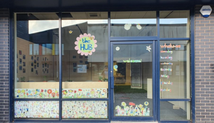 A glass-fronted building with colourful paper murals in the window and a hand-drawn sign saying 'The Hub.'