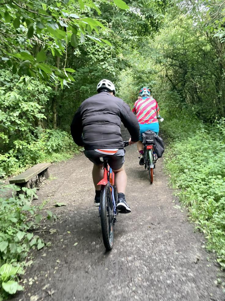 The backs of two people riding bikes along a pathway covered by trees