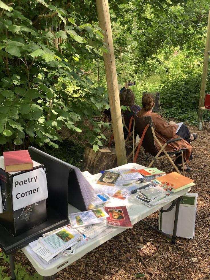 A table with books on it and a box reading 'Poetry corner' surrounded by green trees
