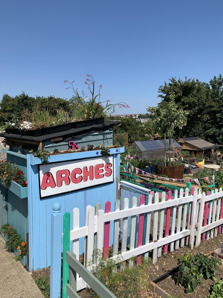 A green area with a colourful picket fence and a sign saying "Arches" on a blue wooden shed.