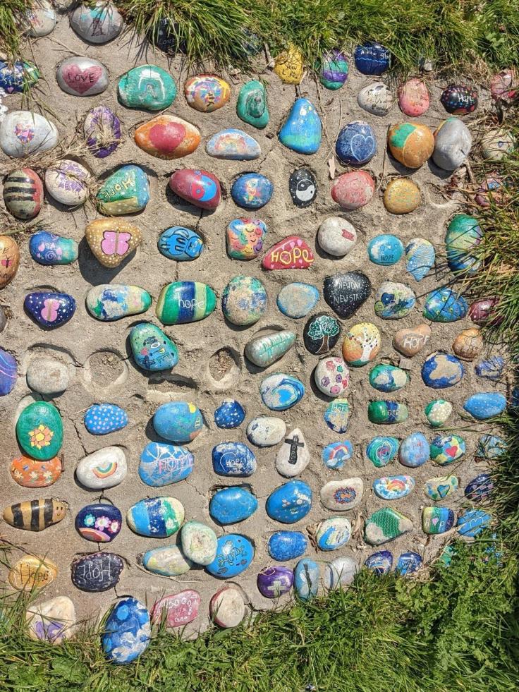 A large group of colourful decorated pebbles in the sunshine.