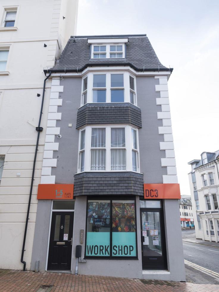 A smart grey end-of-terrace shop front with the word "Workshop" in the windows, which are decorated with artistic designs.