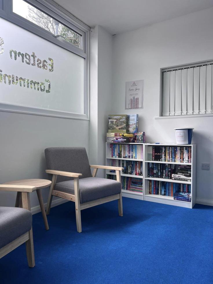 An armchair next to a bookcase filled with books in a white room.