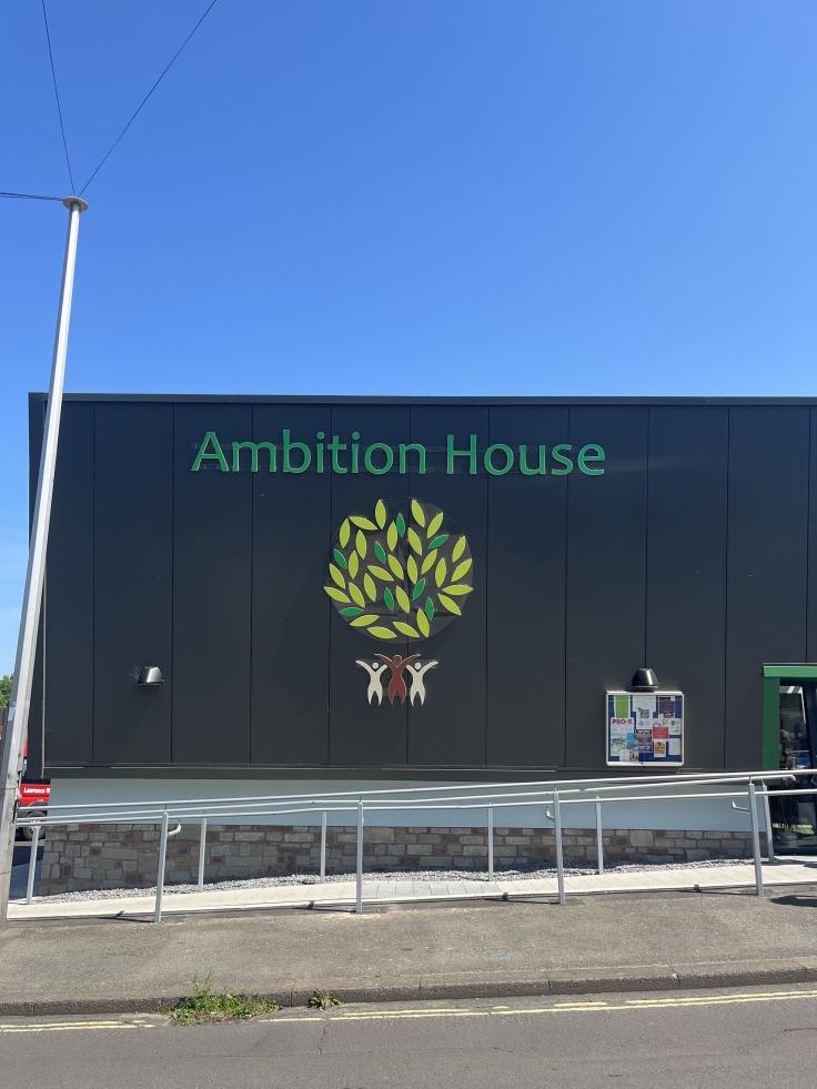 Large black-panelled building with signage reading 'Ambition House' and artwork of yellow and green leaves