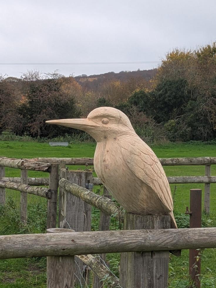 A small wooden kingfisher sitting atop a wooden fence post.