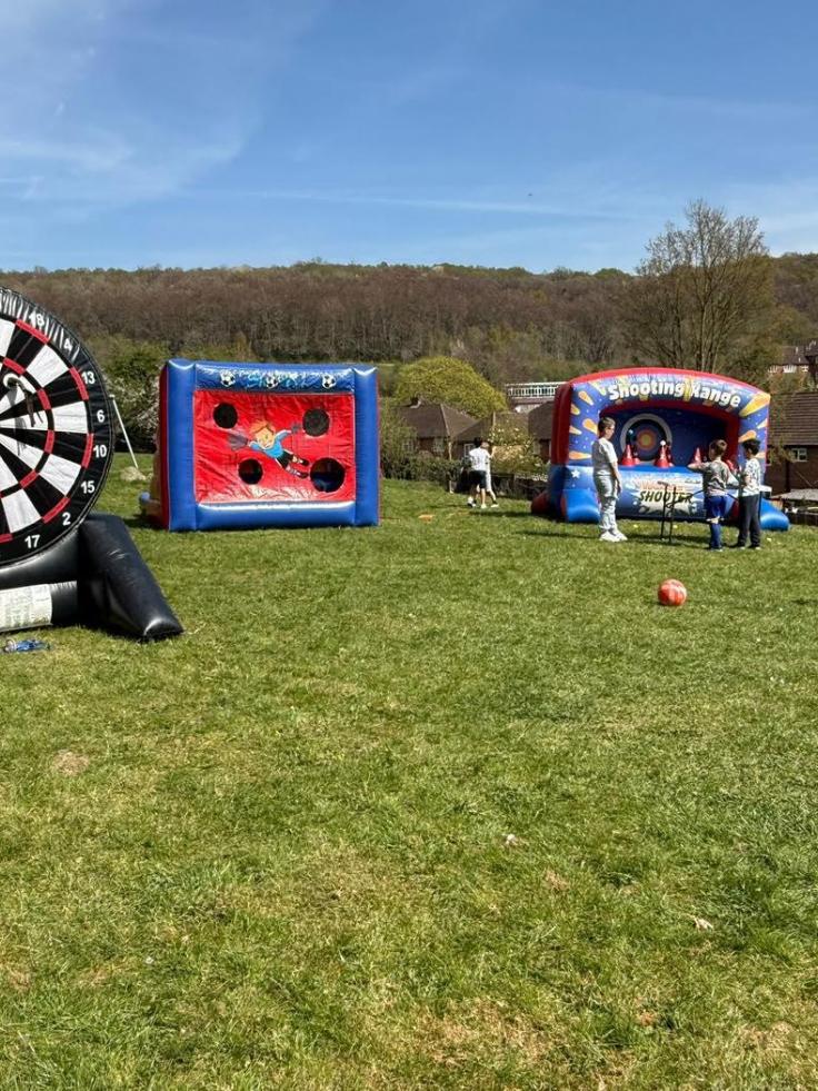 Bouncy castles and inflatable games in a grassy field with woodland in the distance.