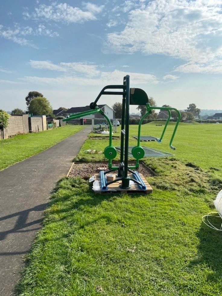 Green-painted outdoor gym equipment in a sunny parkland area.
