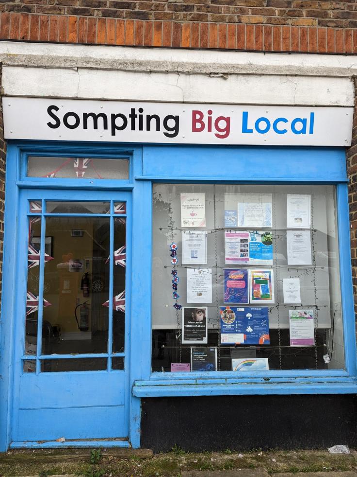 A shop front with a sign above reading 'Sompting Big Local' and a blue-painted front door.