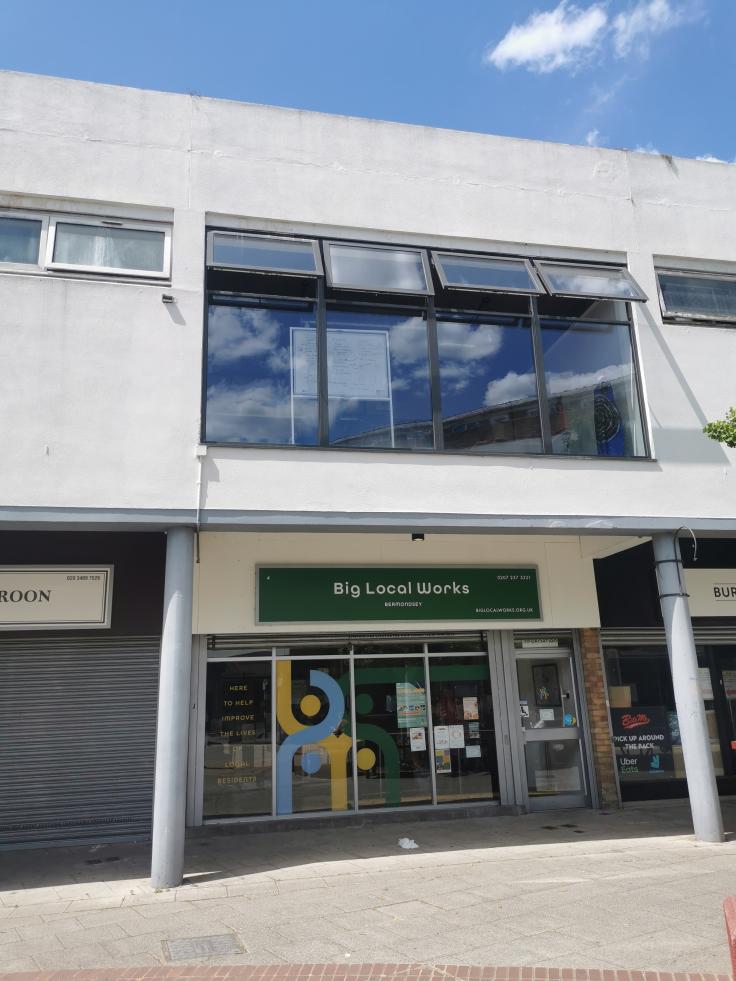 Glass shop front situated under a large white overhanging storey with a green sign reading 'Big Local Works'