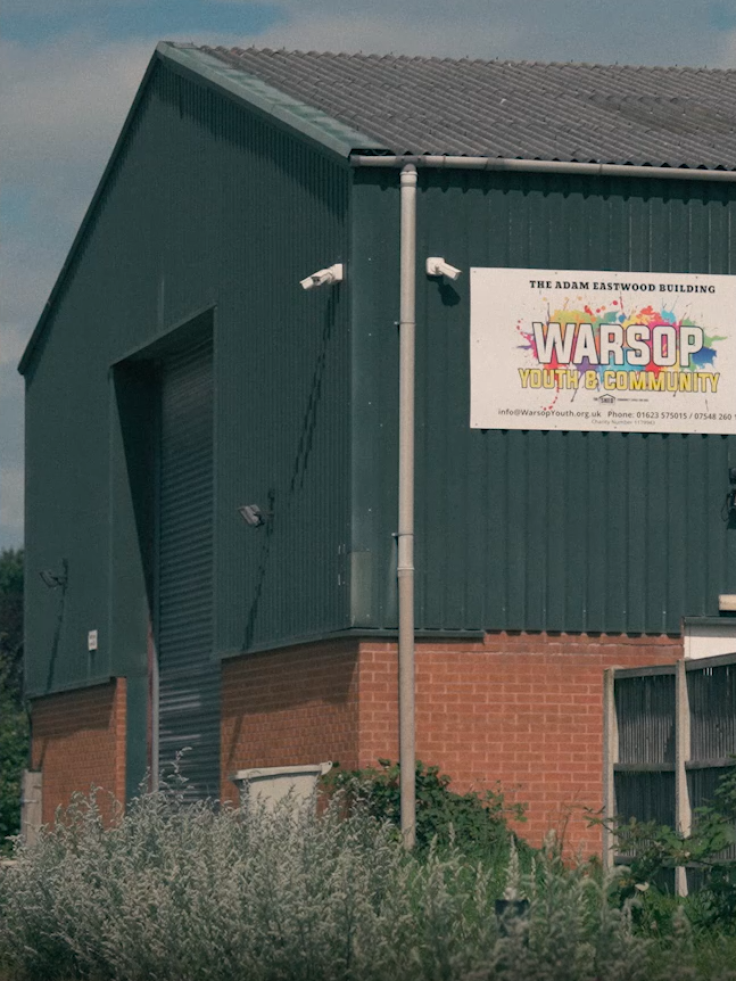 A large industrial brick and green metal building, with a sign reading "The Adam Eastwood Building, Warsop Youth & Community".
