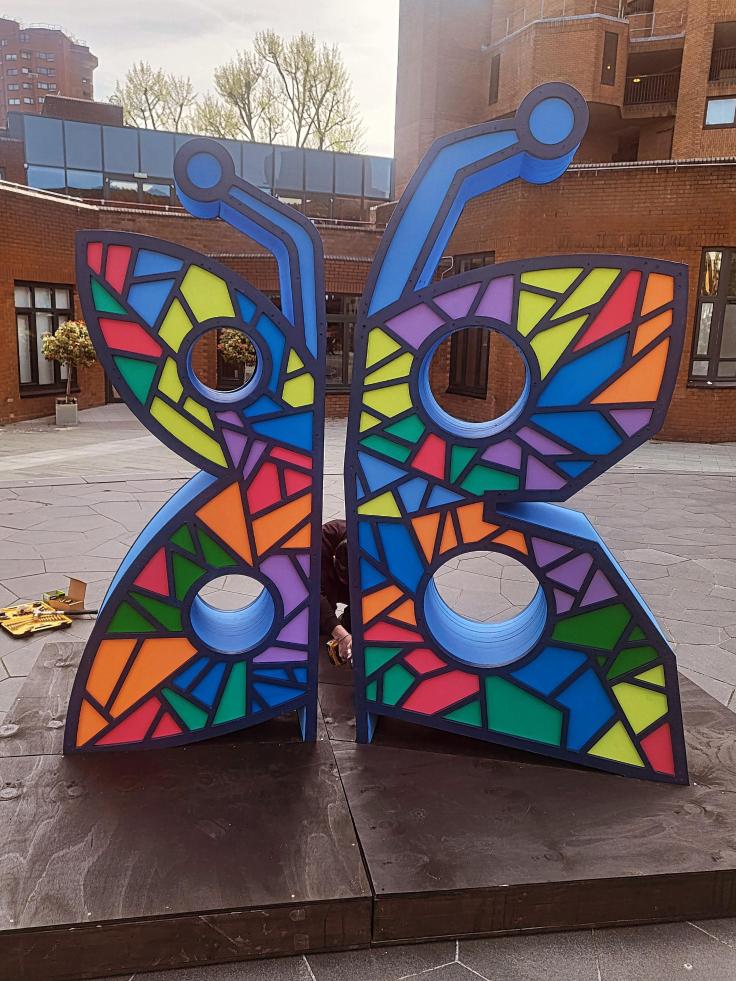 A colourful butterfly sculpture in a square surrounded by brick buildings