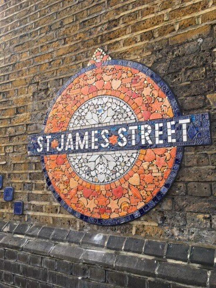 An underground roundel made up of small mosaics in blue, orange and white, reads "St James Street', against a brick wall.