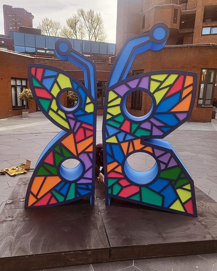 A large bright sculpture of a butterfly, painted with a colourful stained-glass effect.